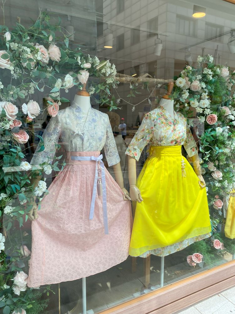 Two brightly colored traditional Korean outfits (hanbok) in a store window.