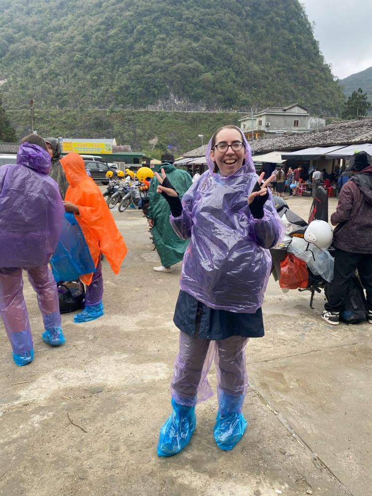 Photo of a woman making a peace sign while wearing a set of purple rain proof clothing.