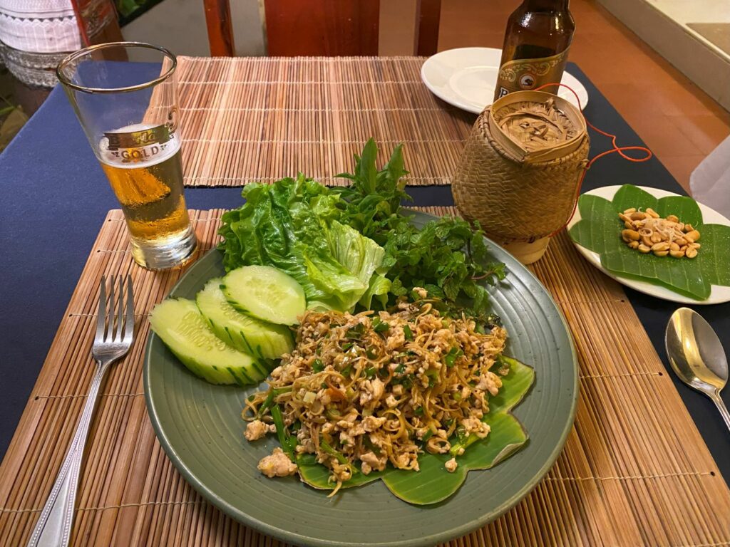 A plate of laap with a small container of sticky rice and a half-drunk glass of beer on either side.