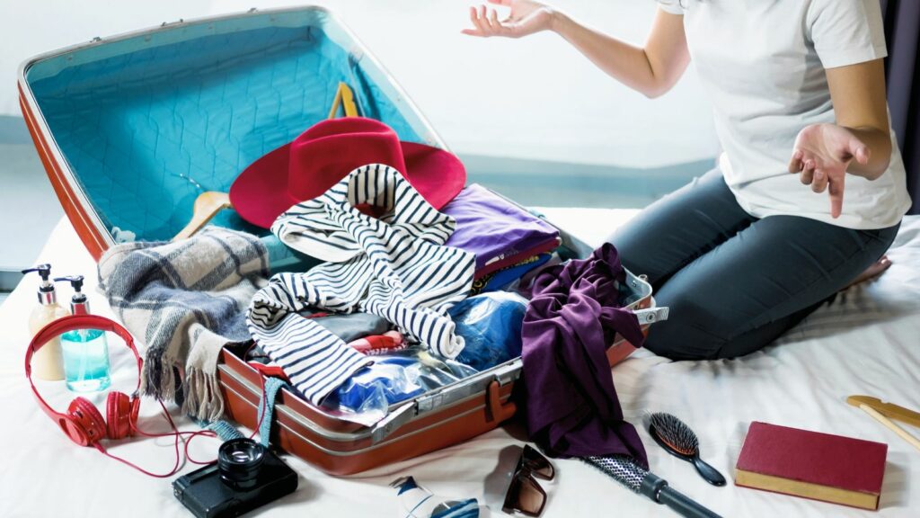 A woman sits looking at her overflowing suitcase, hands held up in exasperation. It's easier to pack when all your stuff is in packing cubes.