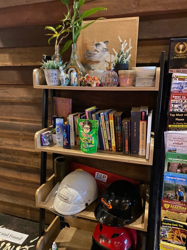 A set of shelves. The top has candles and small jars, the middle shelve has books in various languages, and the bottom has two protective helmets.