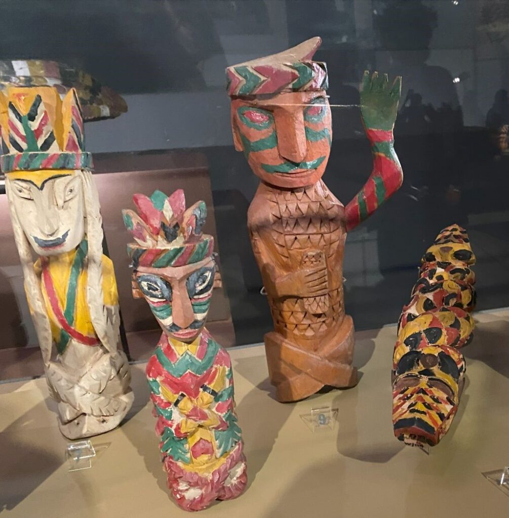 Four wooden carved figures in traditional Borneo outfits, painted in bright primary colors.