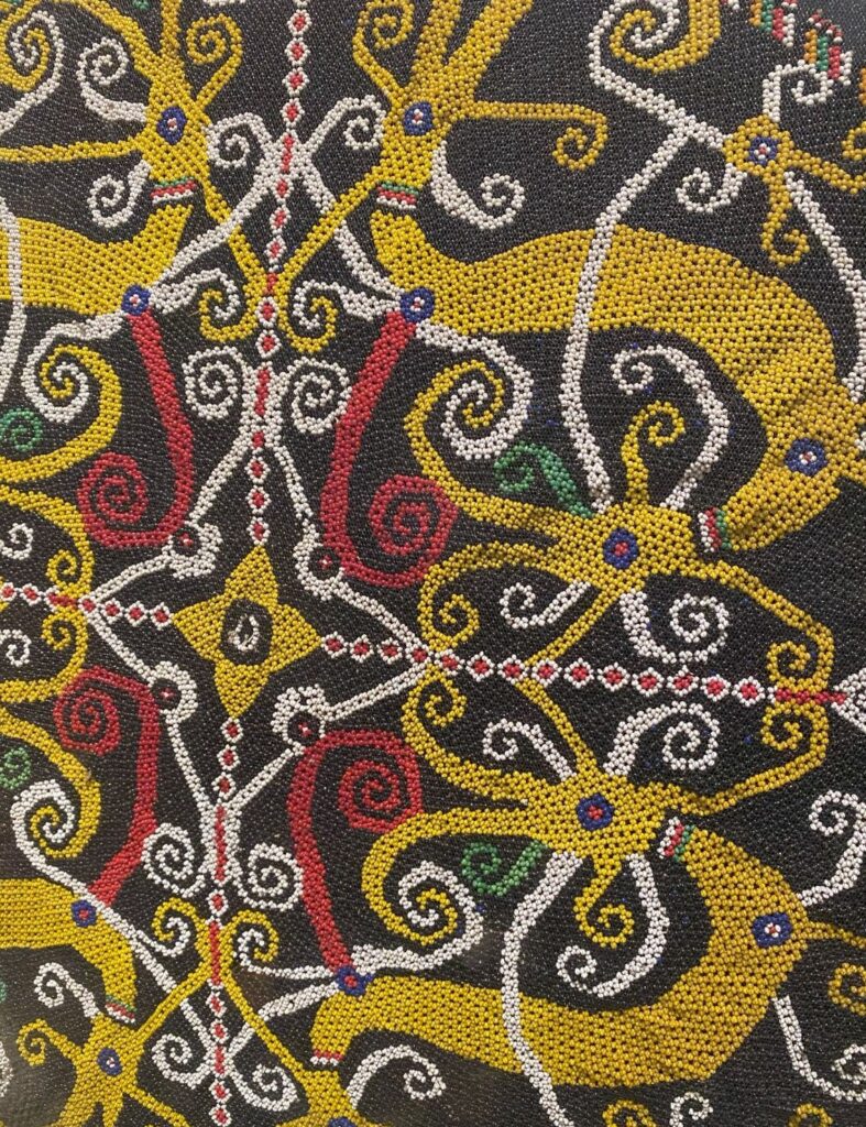 Close-up of a beaded pattern in yellow, red, white, and green colors.