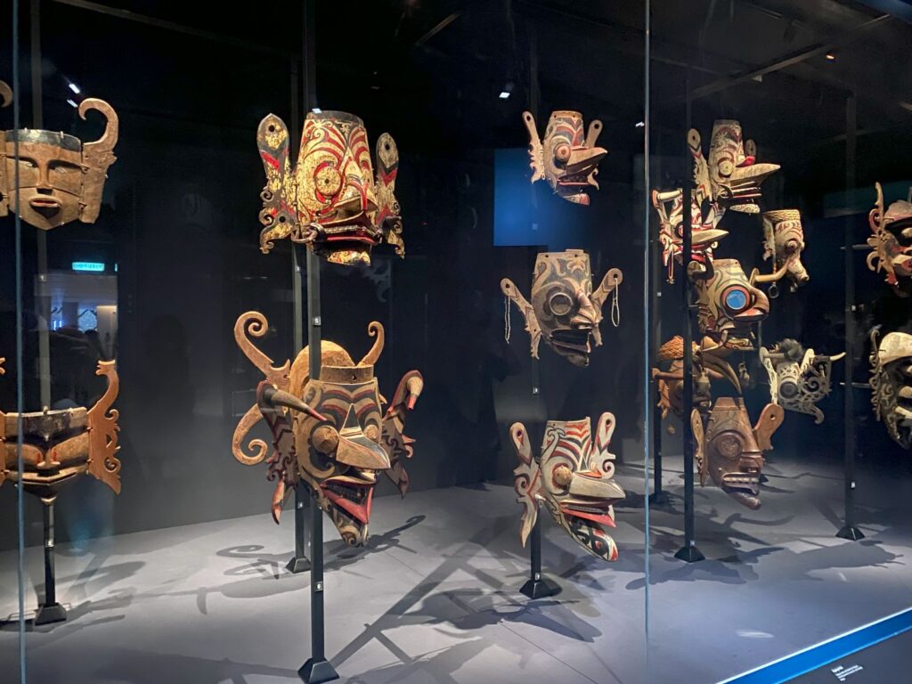 A large selection of carved wooden masks that resemble demons, painted in primary colors.