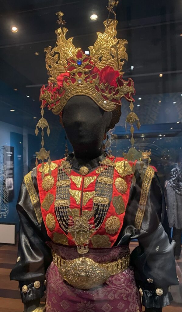 Traditional Borneo tribal wedding outfit with red fabric, metalwork decorative pieces, a large headdress and a matching belt.