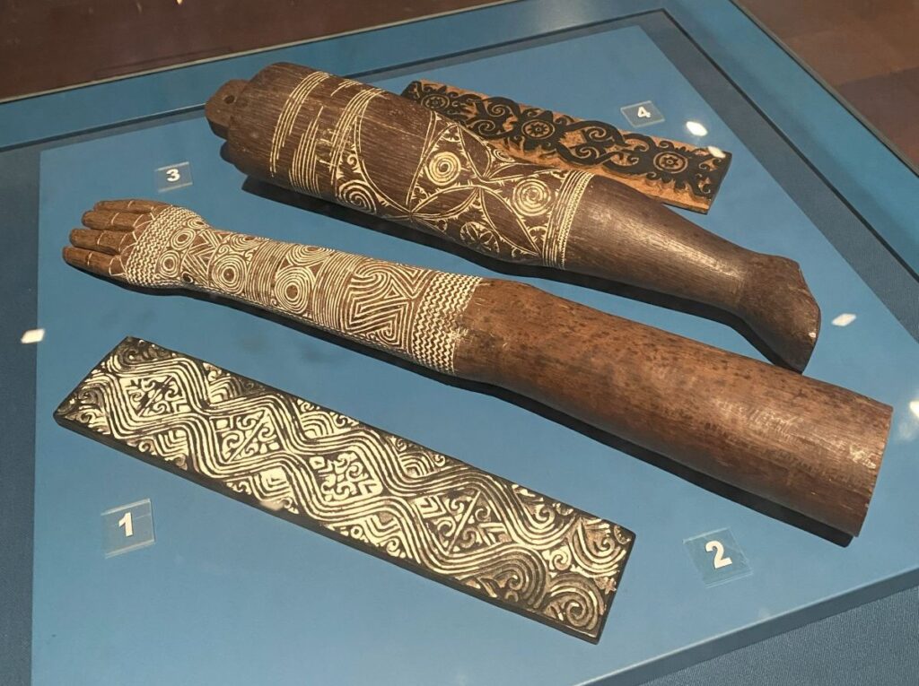 Fake wooden arms with tribal style tattoos painted on them in white ink.