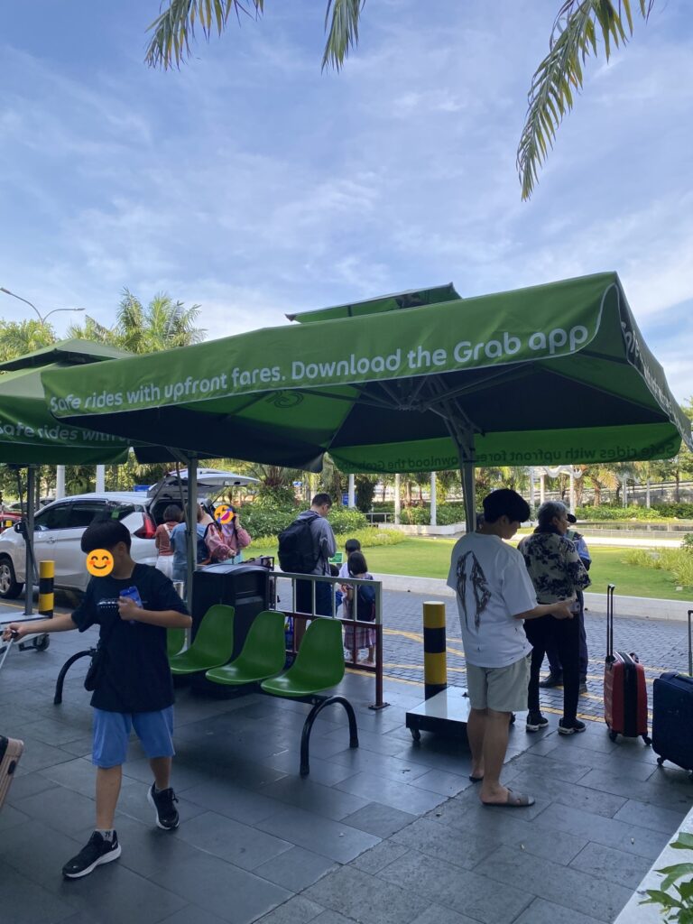 Designated Grab pickup zone at Da Nang Airport, marked with green umbrellas, where travelers wait for rideshare vehicles.